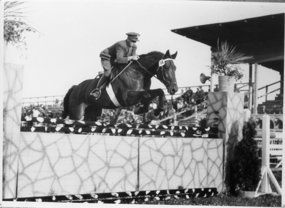 Avfotografert bilde av en militær rytter i sprang over et hinder. Tydeligvis et ridestevne. Rytteren kan muligens være Ottar Markeng som var befal ved Hærens Hesteskole på Starum.