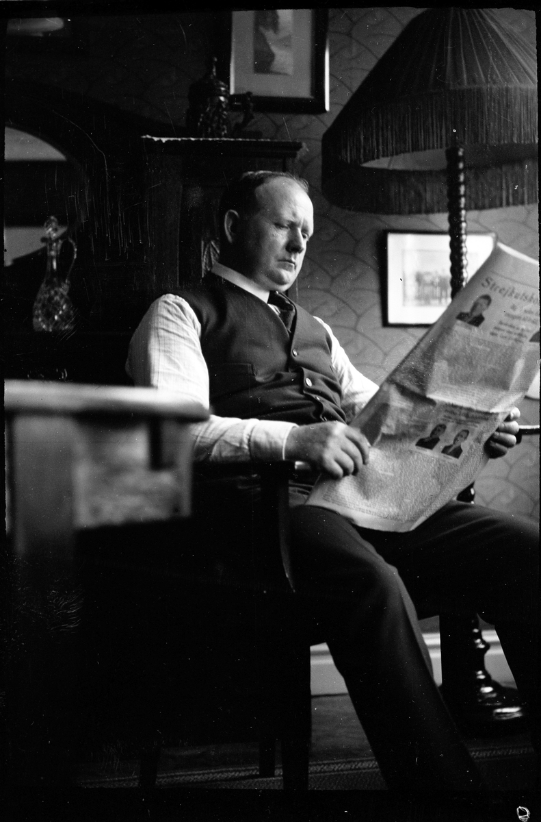 En man sitter i en länstol och läser en tidning.