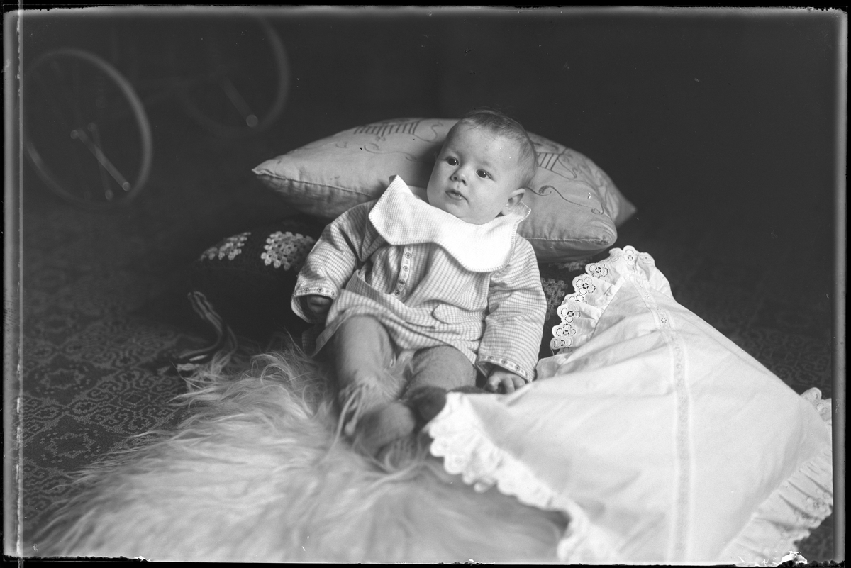 Lars Herbert Pettersson sitter på en fäll, lutad mot kuddar. I fotografens egna anteckningar står det "Sven Petterssons pojke". Bilden troligen tagen i hemmet på Hemvägen 34.