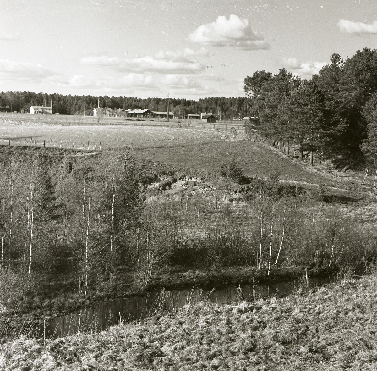 En landskapsvy med åkermark, gårdar och skog vid Glösboån, maj 1964.