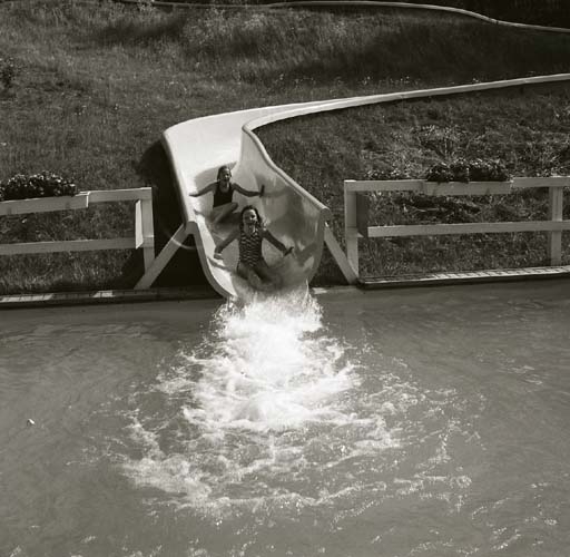 Två barn åker i en rutschkana ned till en vattensamling, 1983.
