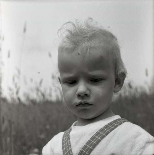 En flicka med hängselklädsel är fotograferad framför ett åkerfält, 1960.