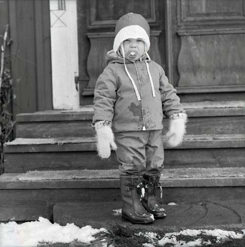 Ett barn står iförd vinterkläder på en trappa, 1975.