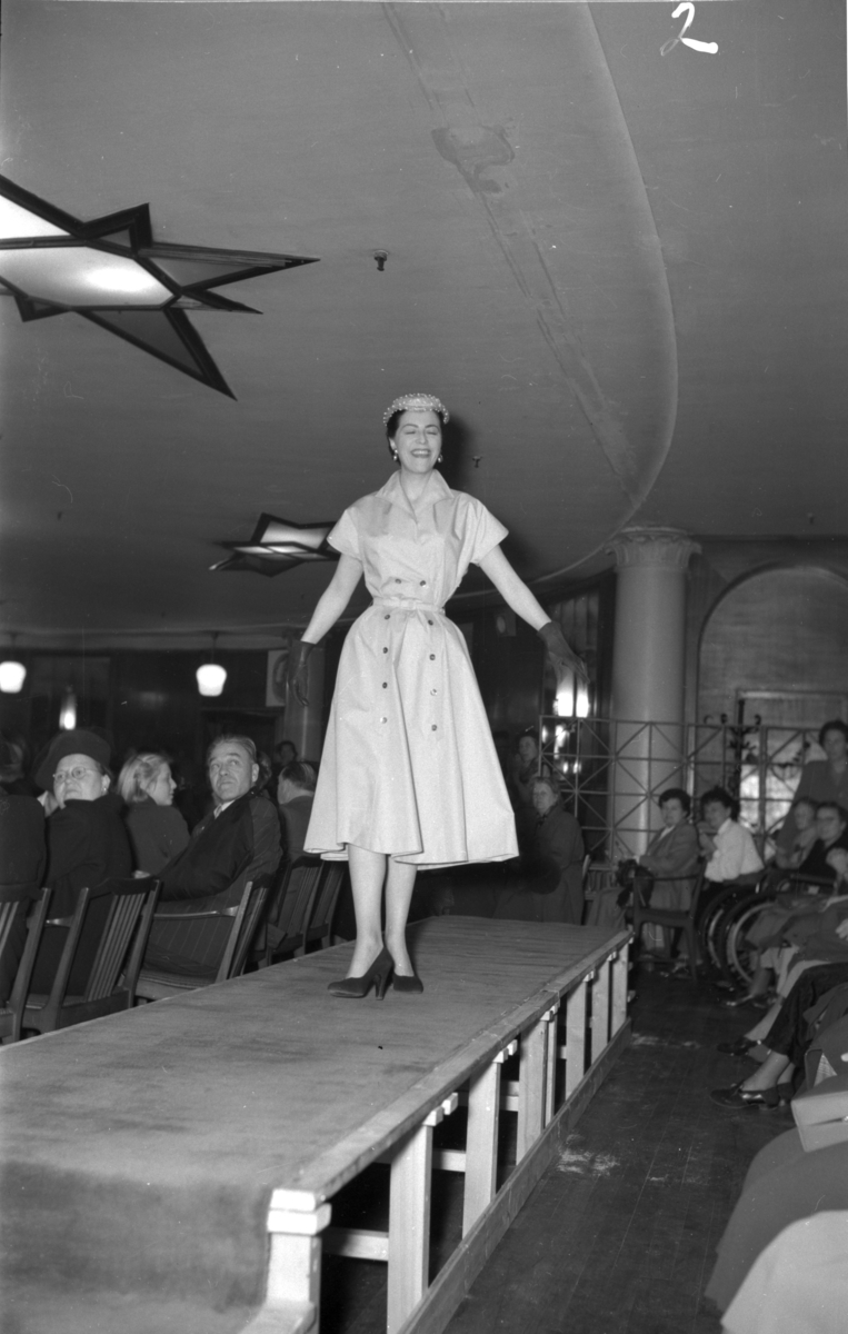 En kvinne på podiet iført kortermet kjole med knapper. Fra en motevisning på Steen & Strøm fra 7. mai 1954..