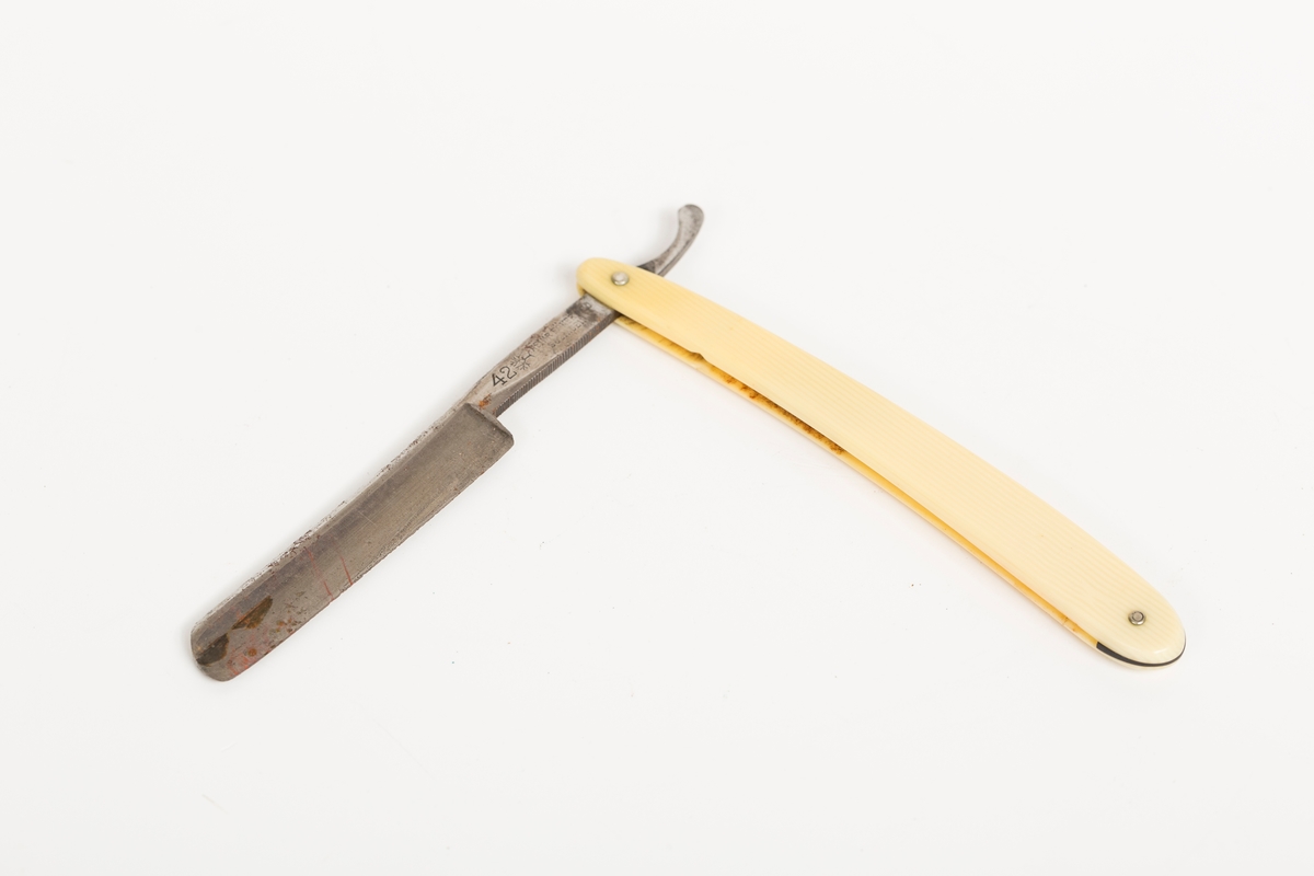 Barberkniv i stål med skaft i gulhvit plast.