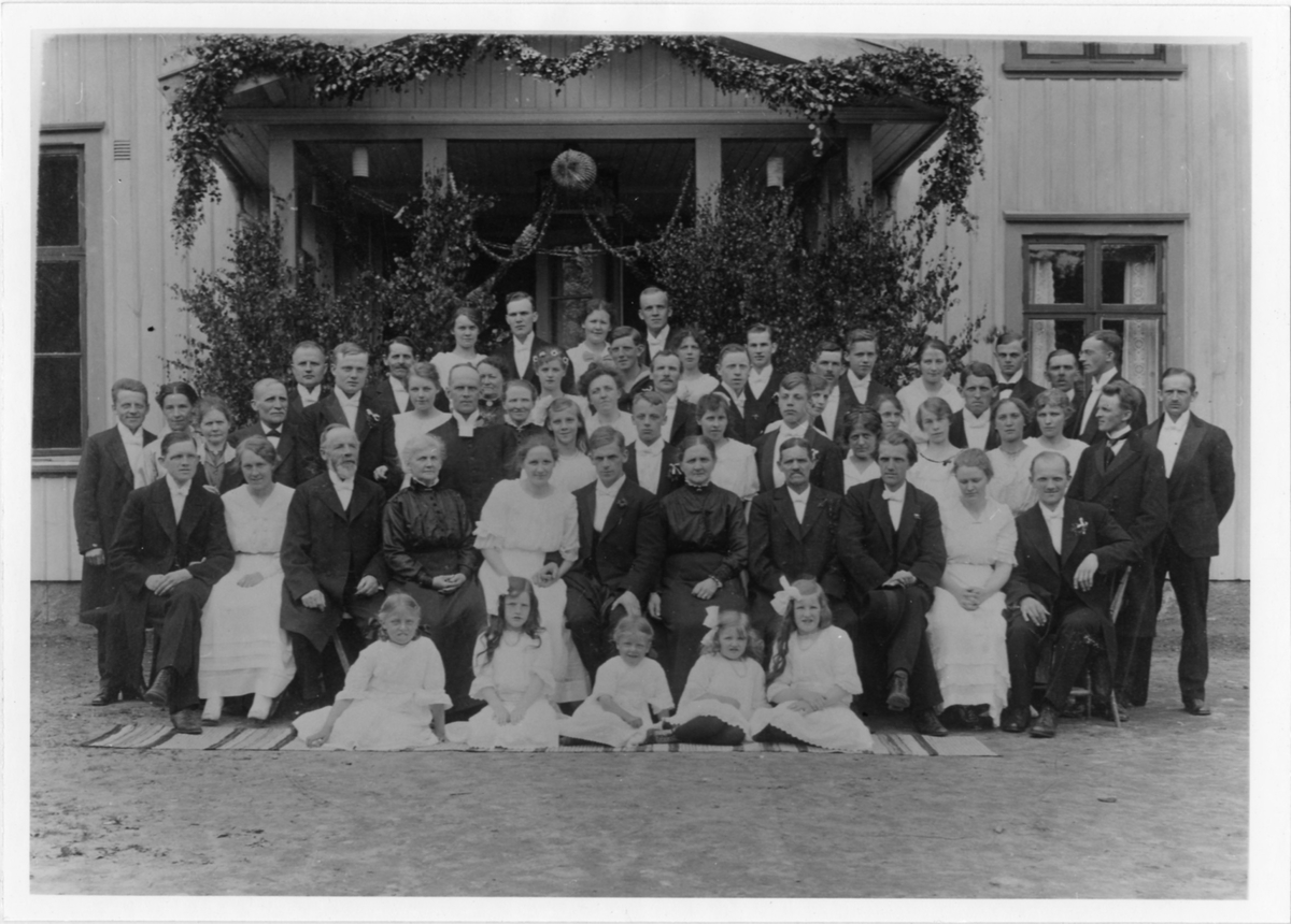 Ett femtiotal bröllopsgäster samt brudparet Nils och Elisabeth Henning utanför skolan i Ödenäs. Nils var lärare i Ödenäs från 1915 och bodde i skolan tillsammans med Elisabeth.