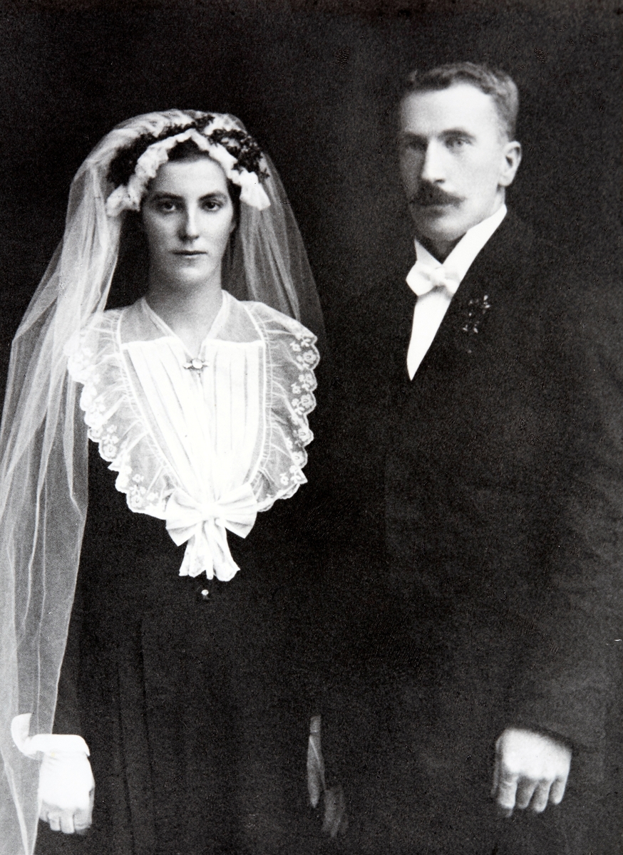 Brudefoto Helga Edvardsen og Even Edvardsen. Bruden har myrt i sløret, svart kjole, hvitt slør med hvitt bryst. Even jobbet som murer.