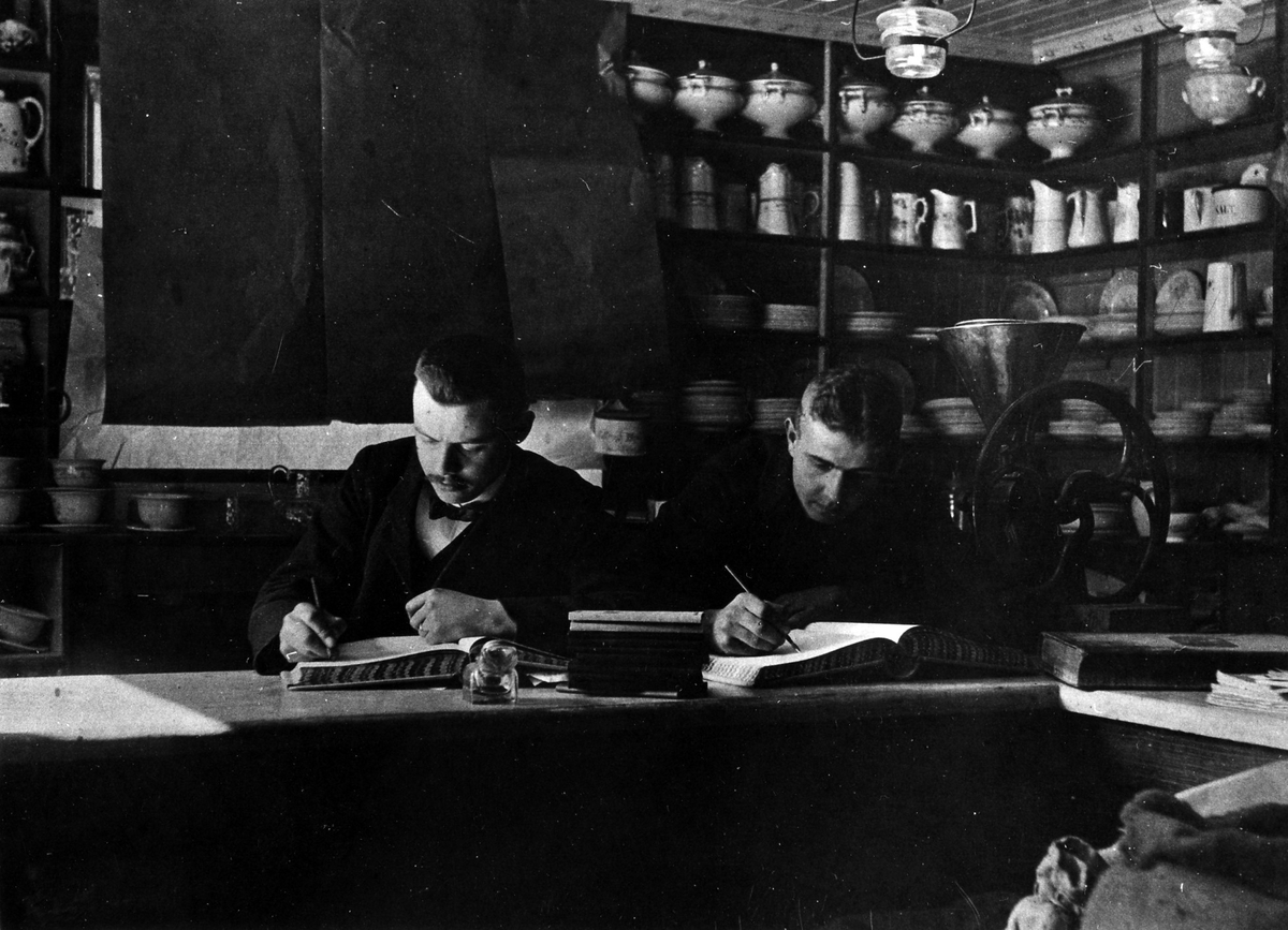 2 män arbetar med någon form av bokföringsarbete vid disken på Melins Specerier. Fr.v: Erik Olsson, Harry Melin.