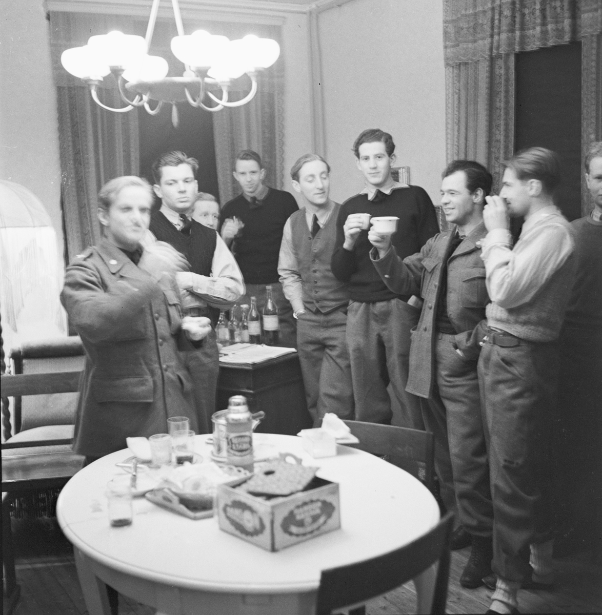 Samkväm på förläggning vid Svenska frivilligkåren i Finland, F 19. Gruppfoto av militärer stående runt ett bord.