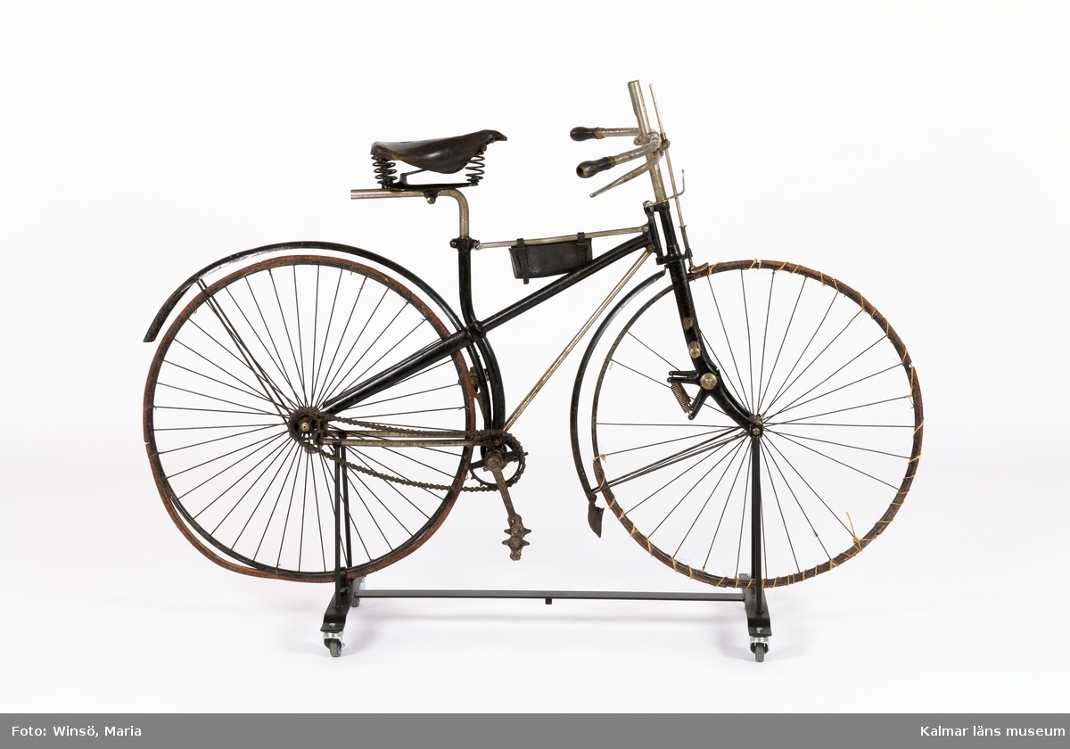 KLM 44079. Cykel. Ram av järn, hjul av stål med däck av massivt gummi och så kallat fast nav. Cykeln (velocipeden), har förstärkt korsram. Framgaffel med fjädring. Kedja med stora länkar, dvs blockkedja. Styret är höj- och sänkbart, med broms, ett äldre patent för konstruktionen, kan ha använts på en föregångare, en damcykel eller en höghjuling. Med cykelväska. Ett stort antal stämplar, bl a olika patent nr, stämpel på metallbleck på trampor: Rudge Cycle Co Ltd, Coventry. Lanserades under benämningen säkerhetscykel. Tillverkad i England, Rudge Cycle, D Rudge & Co Ltd, Coventry. Sadel, tillverkad av Brooks (vilka tillverkar sadlar än idag).