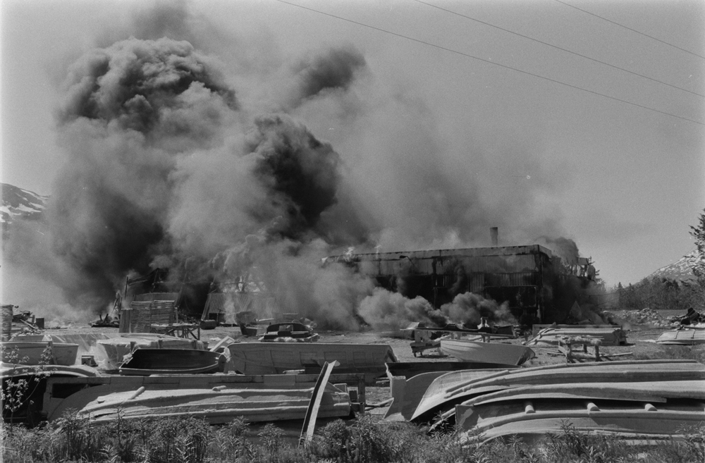 Båtfabrikken Polar-Industri A/S i Drevvatnet totalskadd ved brann 16 Juni 1978. Fabrikken brenner, mye røyk.
Båter og båtformer i forgrunnen.
