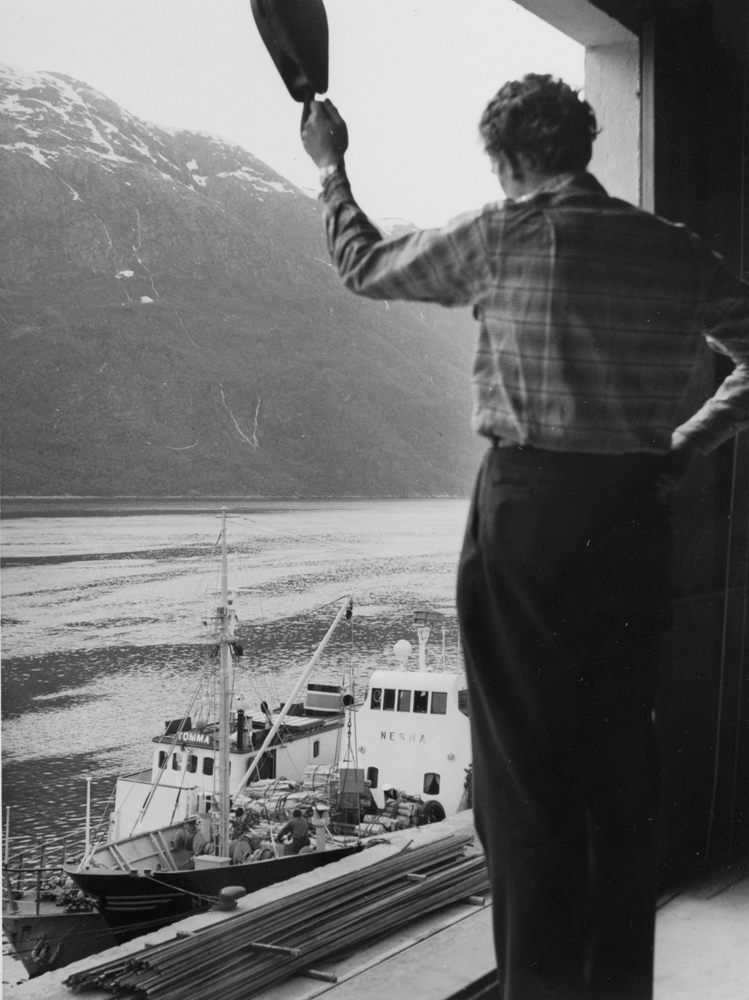Mann i andre etasje på kailageret på jernbanekaia som ser på båter ved kaia. Sjøbusser.