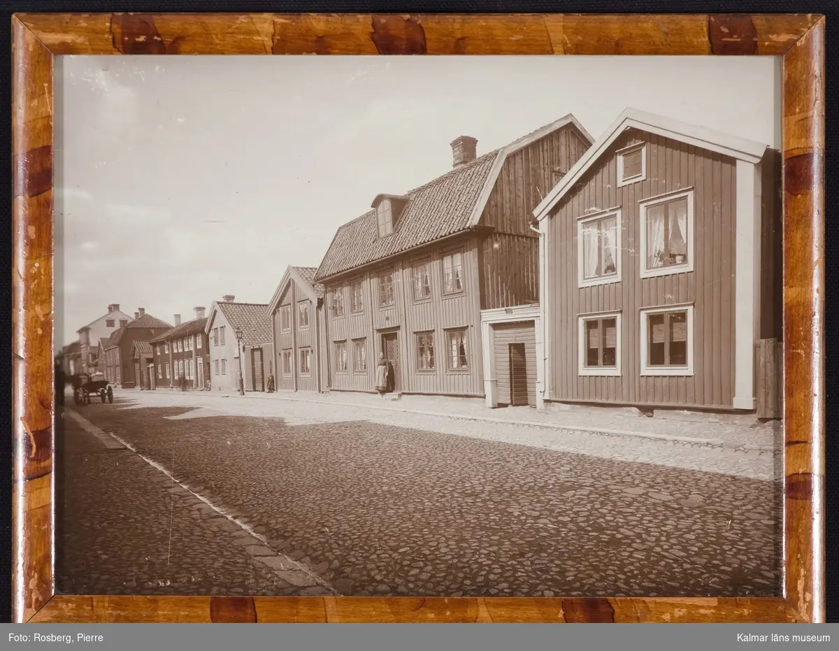 Ett parti av Norra Långgatans norra sida, kv Skoflickaren 10 mfl, gatumiljö med kvinna, barn och hästtransport, gatan och trottoarer, kullerstenslagda.