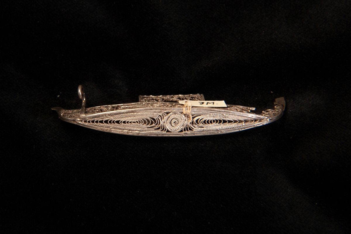 En miniatyrbåt/gondol i filigranarbete i silver. En hängögla finns i skeppets ena del, där den andra öglan troligtvis suttit är filigranarbetet trasigt. Ostämplat.