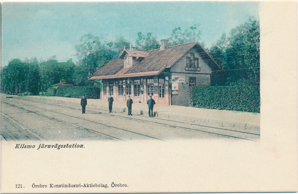 Stationspersonal framför Kilsmo järnvägsstation. Kolorerat vykort från början av 1900-talet.