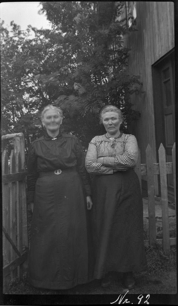 Portrett av to kvinner ved hagegjerde.