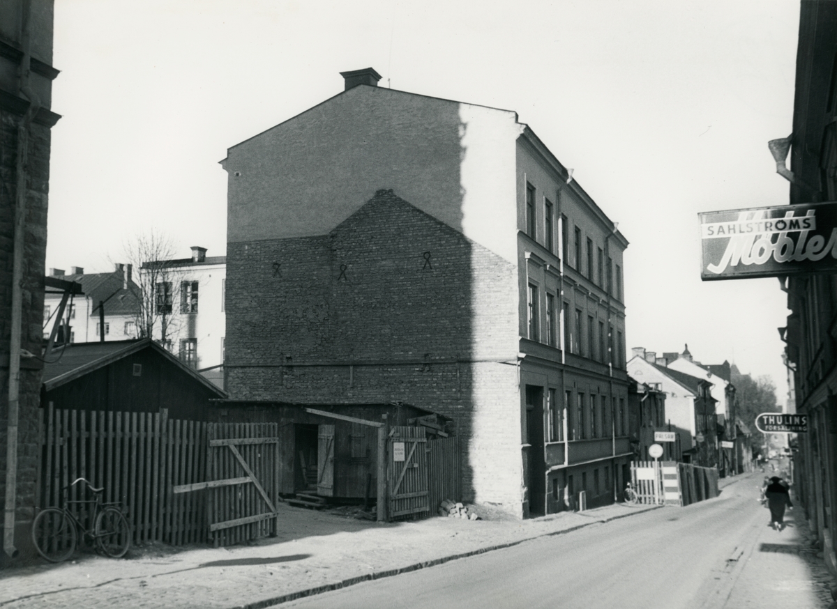 Gatuvy från Tunnbindaregatan i Norrköping. Byggnaden i bild ligger i kvarteret Haken (nr 8), på Tunnbindaregatan 21. Bilden är tagen i samband med rivningsansökan 1956. Vy mot Nordväst.