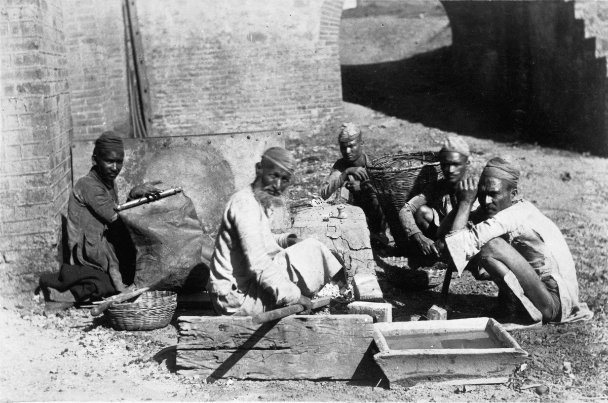 Indiska smeder i arbete vid the Kumaon Iron Works i Indien. Deras utrustning var lätt att flytta.
Från vänster till höger syns bälgen, smeden och tre andra medarbetare med en korg med träkol och en hammare.
Till höger i förgrunden vatten för härdningen.
Foto: Carl Wittenström 1862/63.
