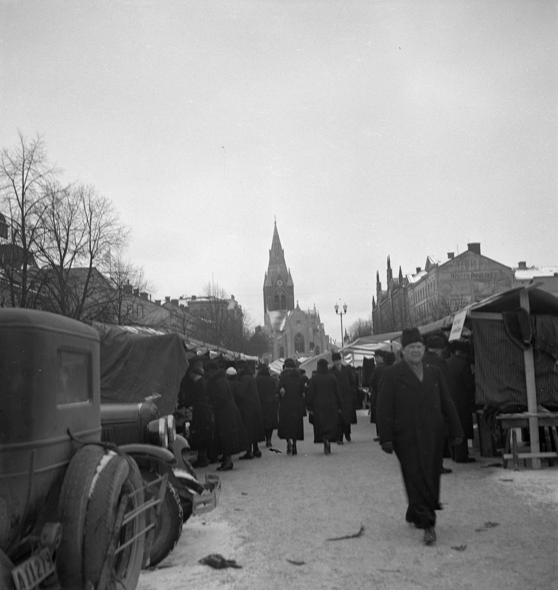 Hindersmässan i Örebro den 28 januari 1937. Människor promenerar mellan marknadsstånden på östra delen av Stortorget. Nikolaikyrkan syns i bakgrunden.