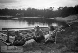 Tre personer ved innsjø i granskog