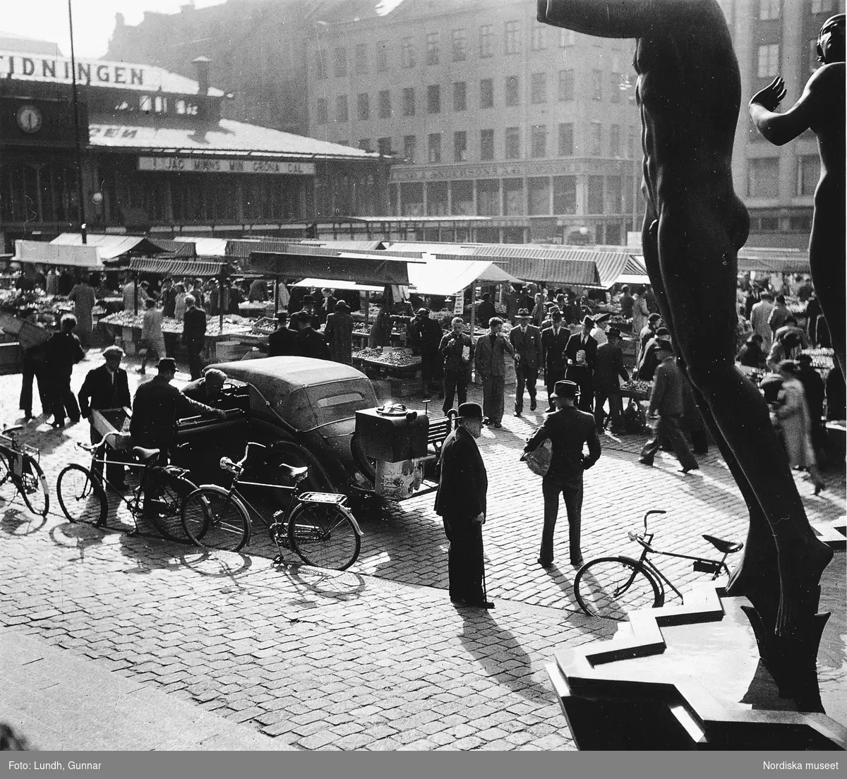 Hötorget i Stockholm år 1942. Torghandel pågår och mycket folk går mellan stånden. I förgrunden en gengasdriven Hanomag årsmodell 1936 med en cabrioletkaross från Ambi Rudd i Berlin.
