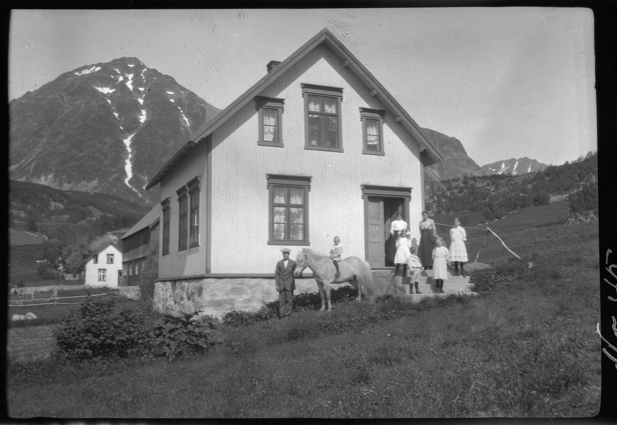 Våningshus med personer og en hest stående foran.