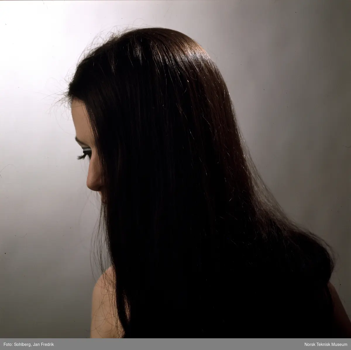 En kvinnelig modell viser fram tidens hårmote. Hun har mørkt, langt hår. Håret dekker nesten hele ansiktet. Profilbilde.