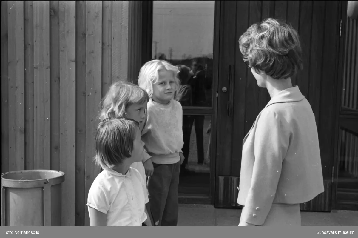 Skolstart i Skönsbergs skola (Hellbergsskolan). Tre små flickor möter sin fröken vid en av de tre, sedermera rivna,  lågstadiepaviljongerna utmed Bruksgatan.