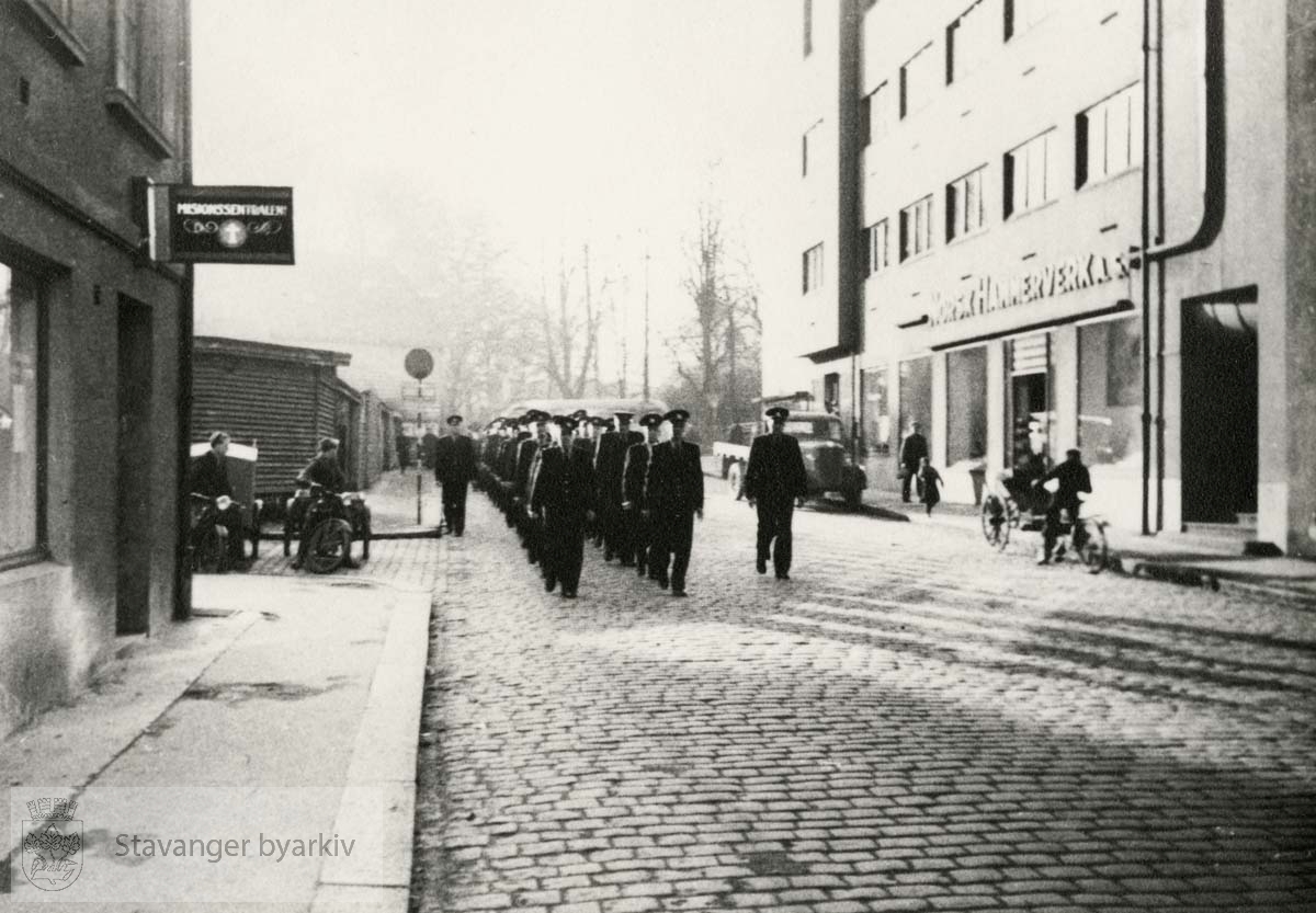 Brannkorpset marsjerer forbi Norsk Hammerverk/ Handelens hus og Misjonssentralen i Klubbgaten.
