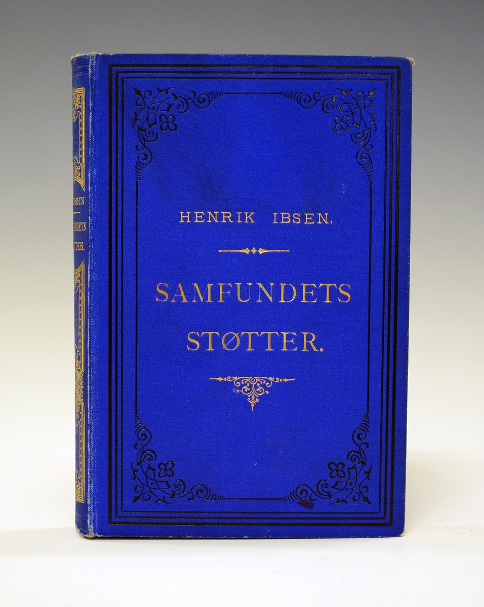 Ibsen, Henrik: Samfundets støtter. Blått helshirtingsbind med preget dekor i gull og sort, helt gullsnitt. 
Andre opplag 1877.