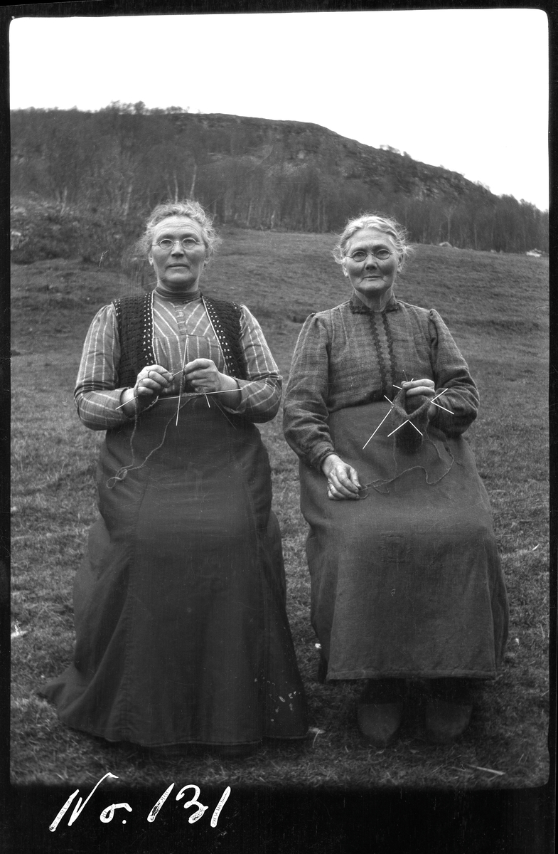 Portrett av to eldre damer som sitter og strikker utendørs.