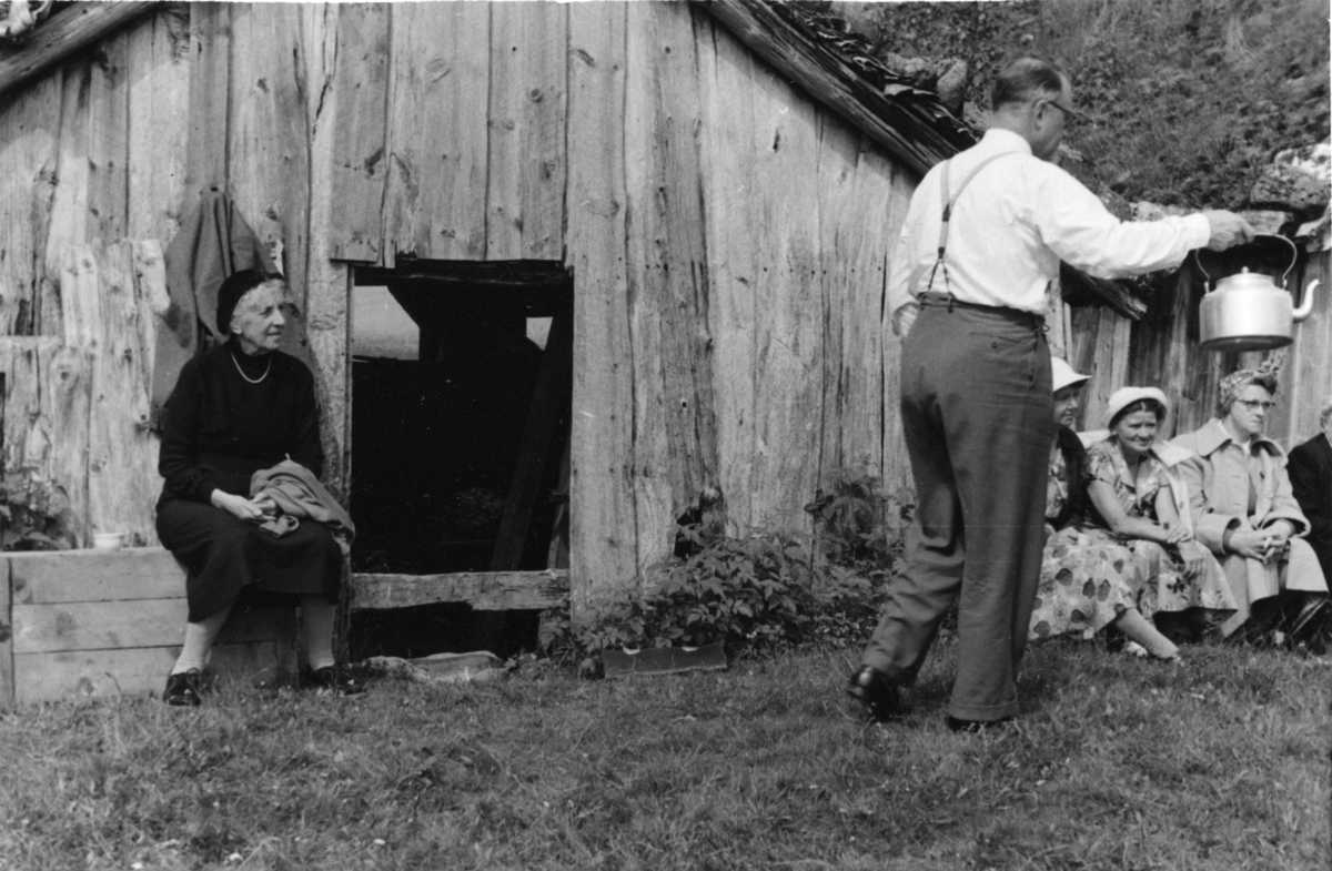 Presten i Suldal og en gruppe kvinner drikker kaffe bak naustene i Kvilldal. De er på utflukt fra Lindum. På bilde 2 står Frida Johannessen og snakker med presten. På bilde 3 sitter Frida Johannessen til venstre, mens presten holder kaffekanna til høyre.