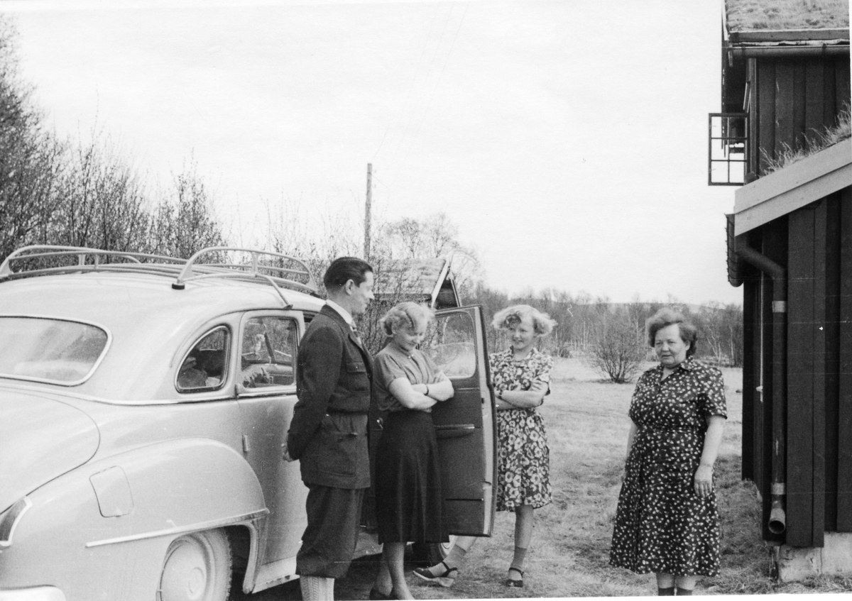 Tre damer og en mann ved bil på gårdsplass