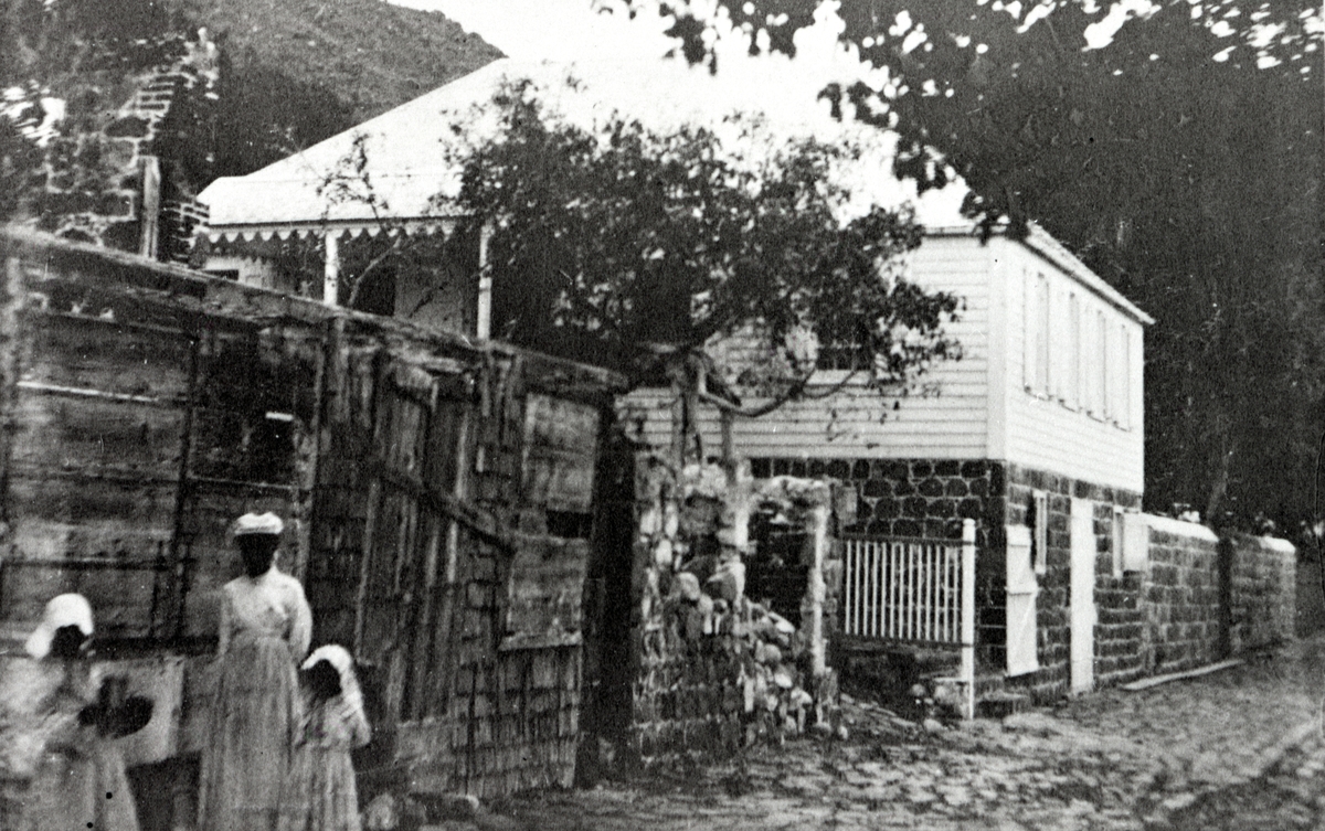 Gatubild från Gustavia. En kvinna med barn står utanför ett bostadshus.