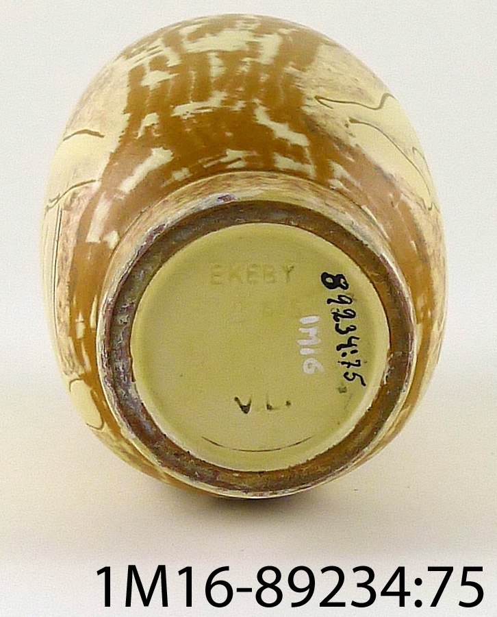 Vas av keramik i gult och brunt, kvinnofigurer på sidorna. Märkt "Vicke" Ekeby VL. Initialerna står för Vicke Lindstrand.