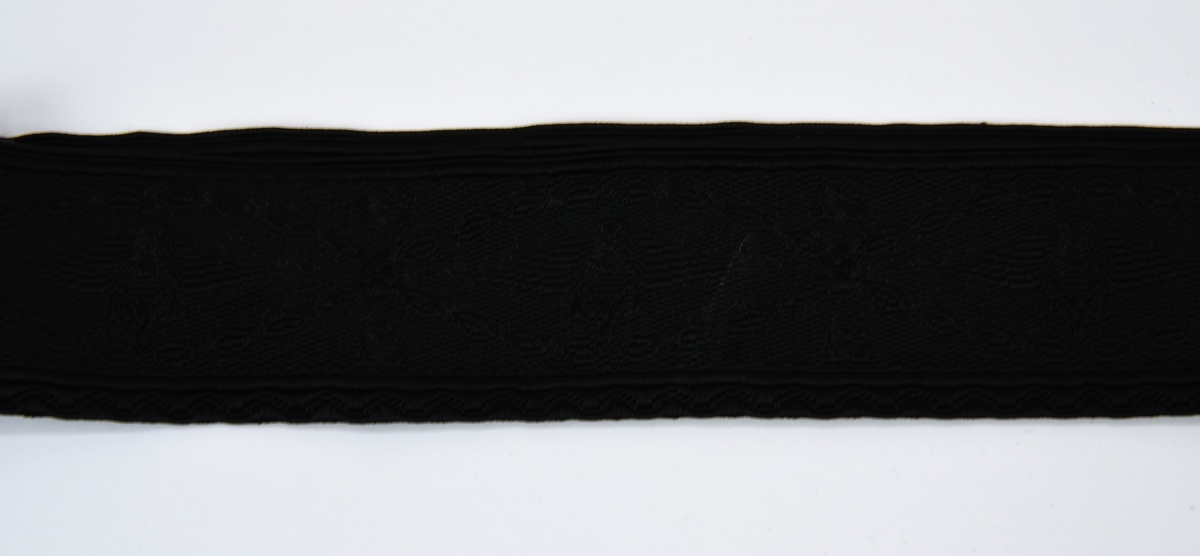 Ett mössband av svart mönstervävt tyg som fästs med kardborreband. Mönstret består av SJ:s bevingade hjul samt SJ:s logotyp i upprepande mönster.