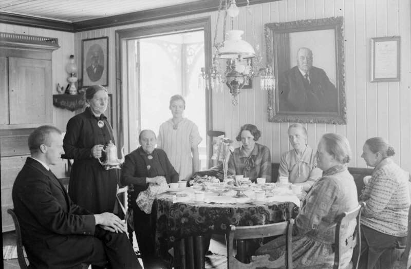 Ringebu. Elstad. Familieselskap, åtte personer, rundt kaffebordet. Anna Elstad med kaffekanne. Portrett av  O.Chr.Elstad på veggen bak.