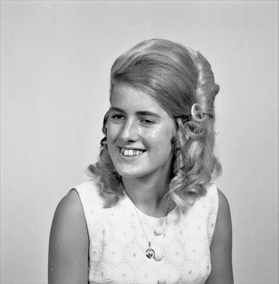 Portrett. Ung kvinne med langt lyst oppsatt hår iført lys sommerkjole med blomstermønster. Smykke i kjede om halsen. Bestilt av Solveig Hansen. 5523 Smørsund.