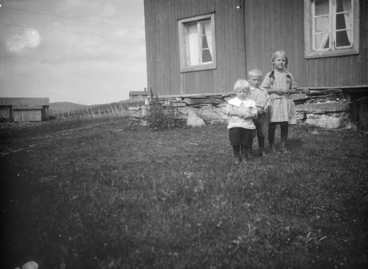 Tre barn foran et våningshus på ukjent gård
