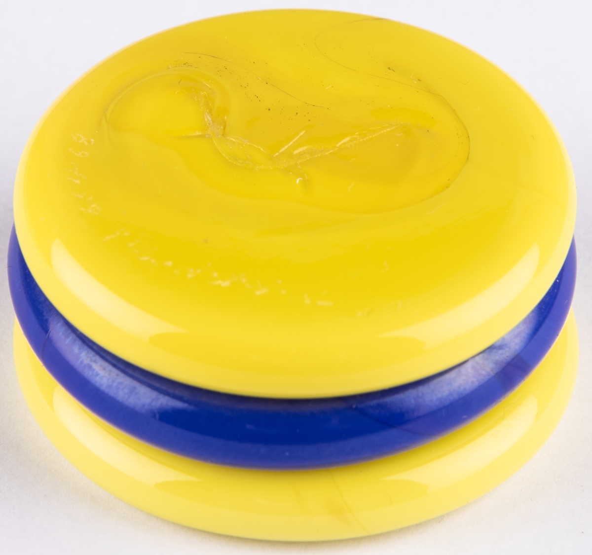Brevpress, småkaka, i kristall. Uppbyggd av tre cirkelrunda hopfästade plattor i gult, blått, gult. Orrefors glasbruk, design Gunnar Cyrén.