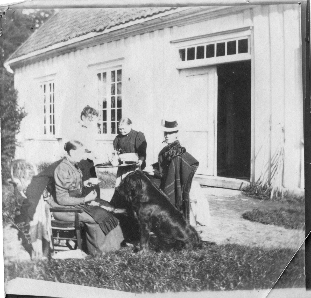 Kaffeservering av Jensine Amundsen til tre kvinner rundt et bord ved kjøkken inngang på Berg. Stor hund, Bamse ? ser på.