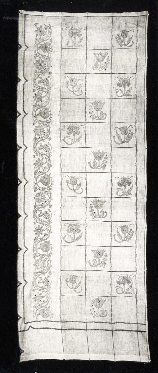 Foto (svart/vitt) av en gardin, broderad på linne, med blomstermotiv i rutor m.m.

Inskrivet i huvudbok 1983.