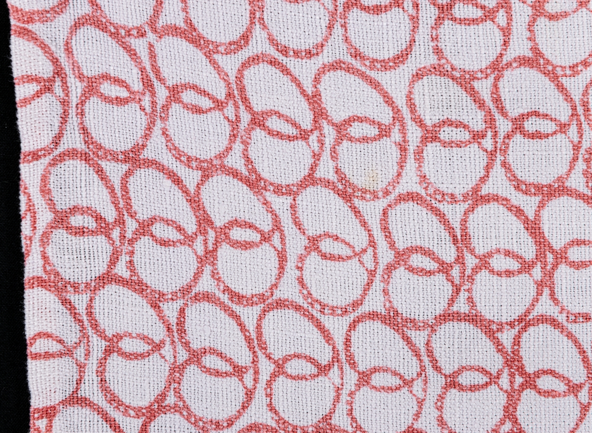 En gardinvåd av bomull med handtryckt mönster, rött mot vit botten. Kallas "Kringlan" eftersom mönstret är i form av kringlor. Vävt av Jobs i Leksand för Gefle Ångväveris räkning i slutet av 1940-talet eller början på 1950-talet. Några fläckar.