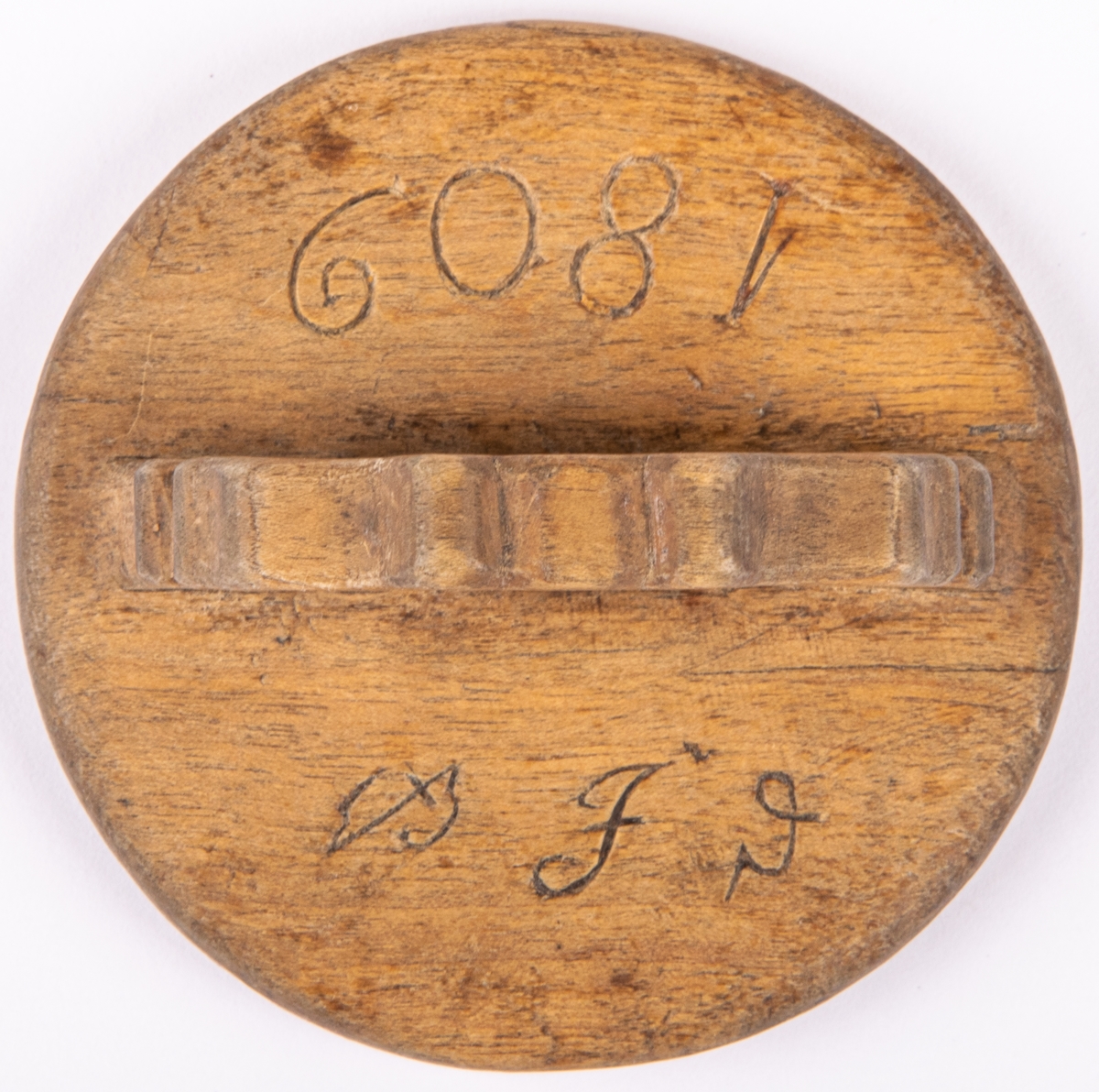 Messmörskrus av trä. Rund skiva med mönstrad stämpelsida, geometriska mönster med uddsnitt och karvsnitt. På ovansidan litet handtag och märkt: BIS.1809.