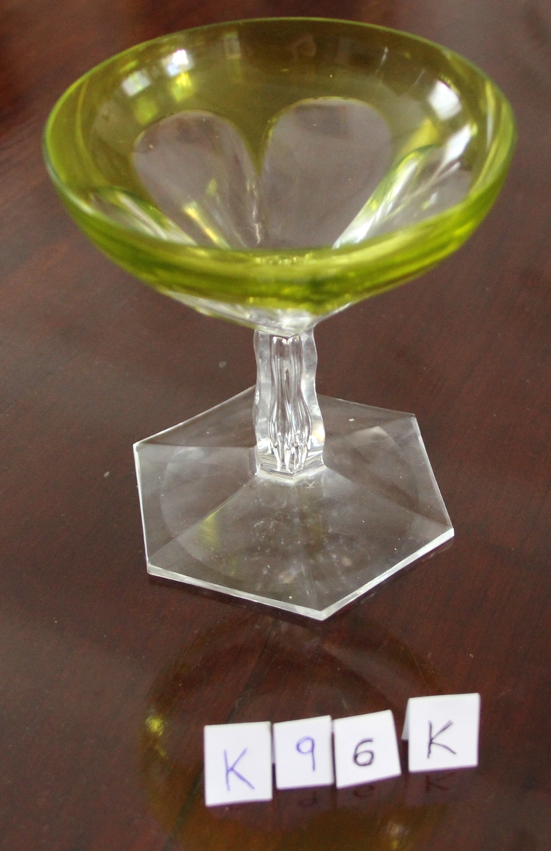 Glass med sekskantet fot, stetten litt innsnevret på midten, skålen har sekspæreformede fasetter, sett ovenfra som en seksbladet blomst.