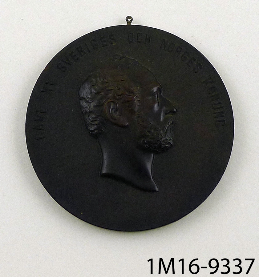 Medaljong föreställande Carl XV Sveriges och Norges konung, av svart ebonit, som är en slags plast.