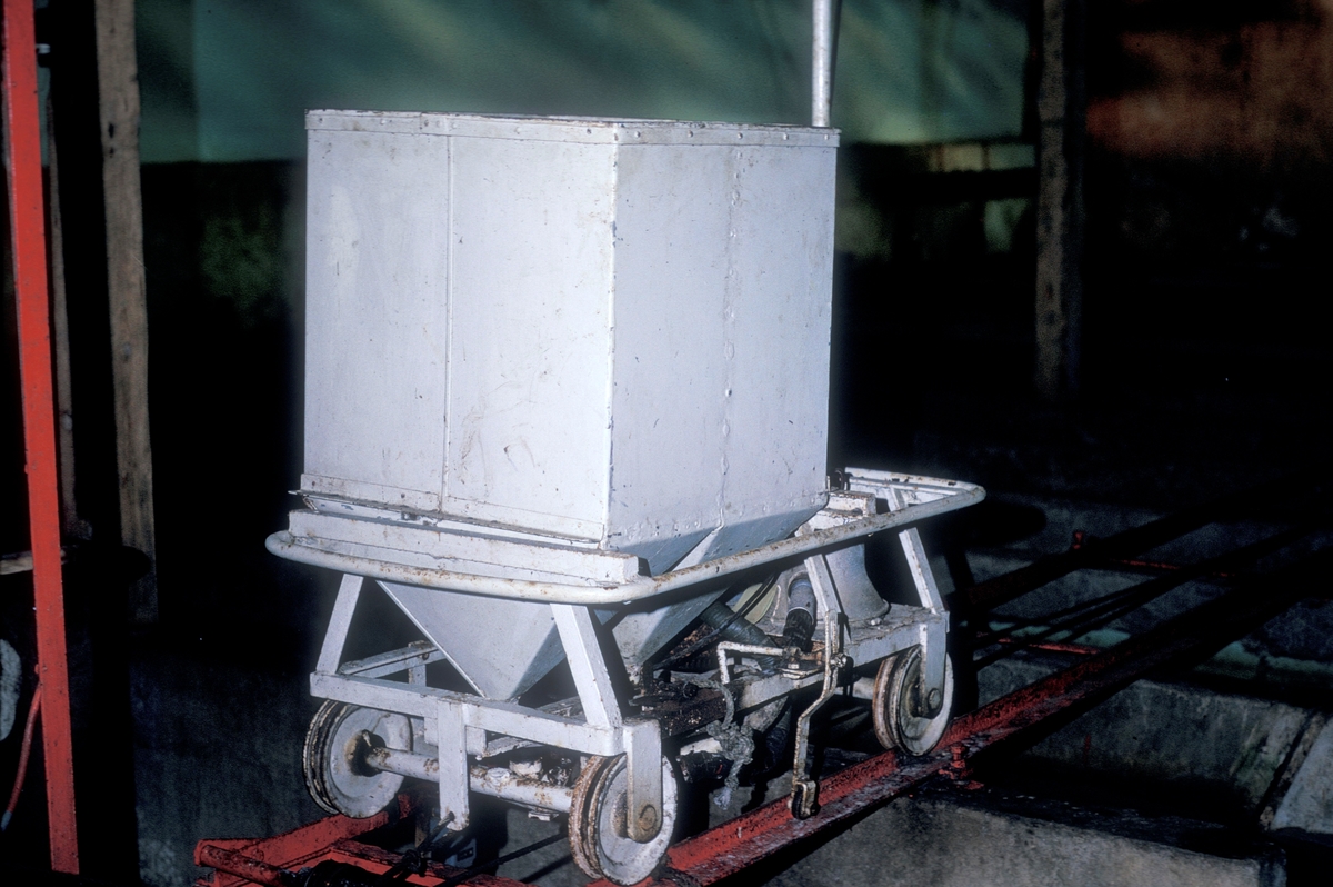 Vogn som går på skinner, montert over betongkummer. Vogna har en stor kasse som ender i en trakt nederst. Vognen kan flyttes fra kar til kar og brukes til å fôre fisken.