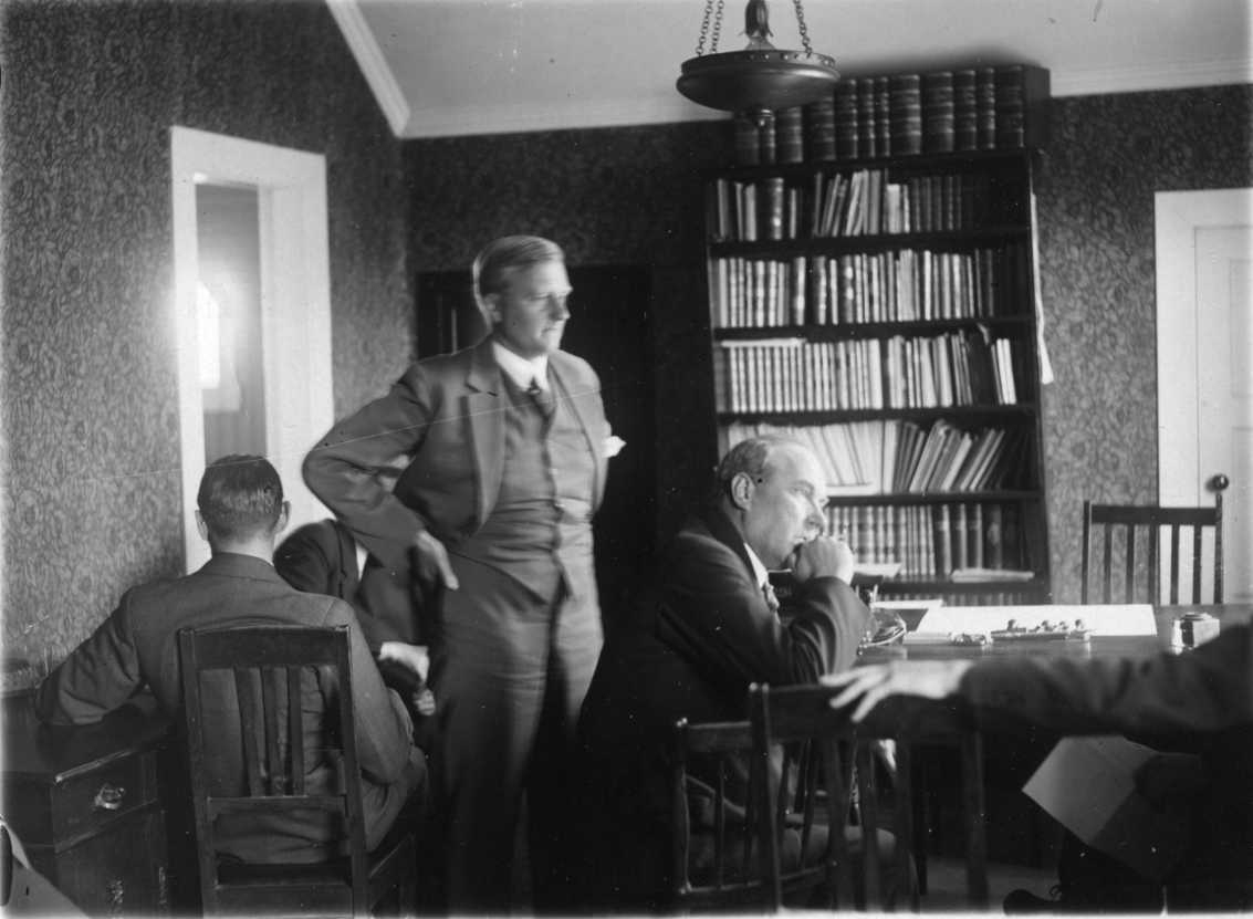 Män i två grupper sitter runt bord. I mitten står en man vänd mot ett samtal till höger. Intill honom sitter Lithberg inbegripen i samma samtal med någon utanför bild.