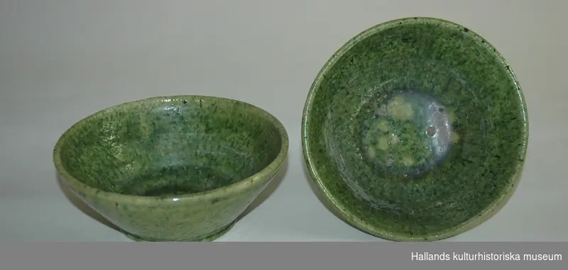 Handdrejad skål av lergods. Grön glasyr. På undersidan skrivet: "Aug. Cederholm keramik Garanteras handarbete Warberg." Nedre diameter:90 mm. 