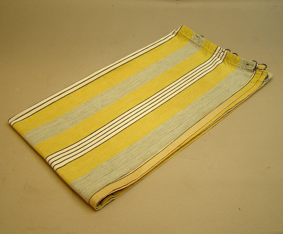En gardinluft bestående av två stycken längder, bomullstyg med mönster av ränder av olika bredd i färgerna: gul, grå, svart, vit. I ovankant är ringar av metall fastsydda för upphängning.